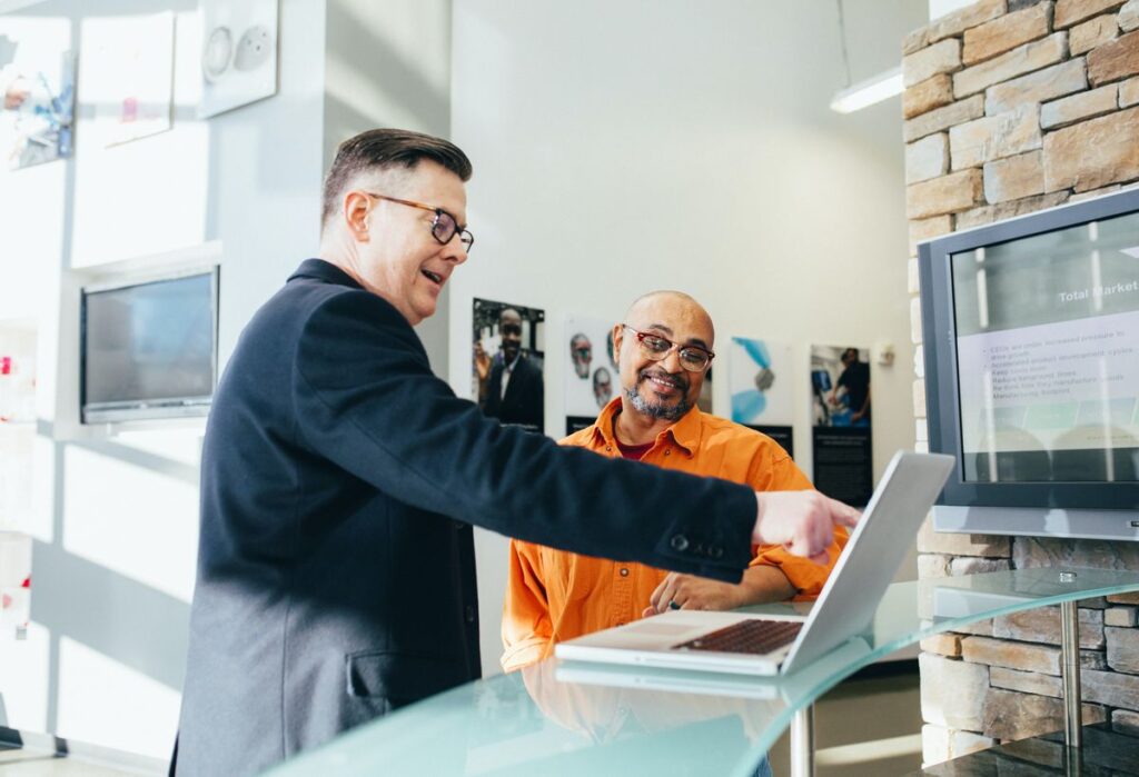 A picture showing two men, and one of them is pointing to a laptop.